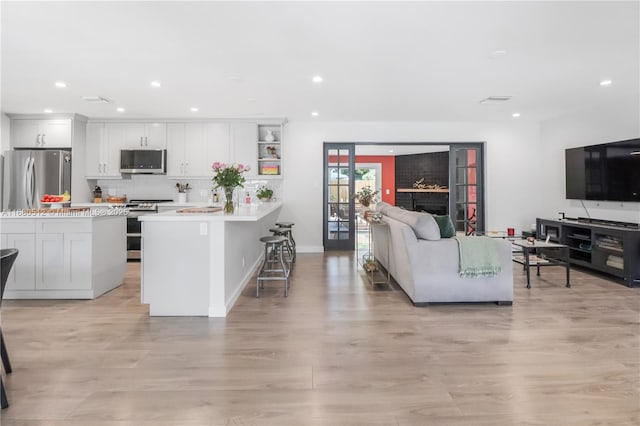 kitchen featuring white cabinetry, backsplash, light hardwood / wood-style floors, a kitchen bar, and appliances with stainless steel finishes