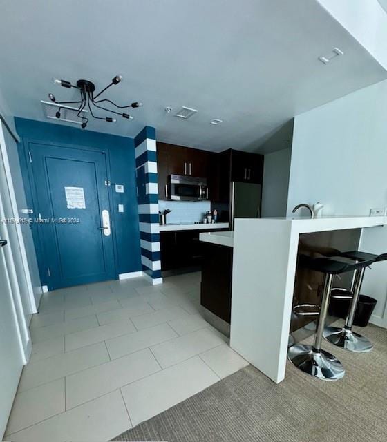 kitchen featuring light tile patterned floors, refrigerator, a kitchen breakfast bar, decorative backsplash, and an inviting chandelier