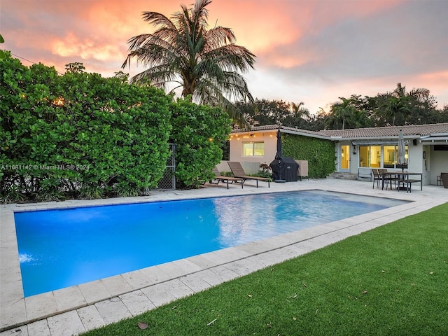 pool at dusk featuring a patio area and a yard