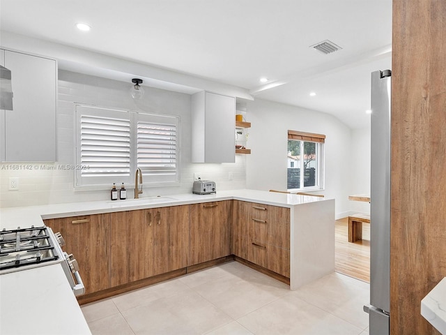 kitchen with kitchen peninsula, decorative backsplash, stove, sink, and stainless steel fridge