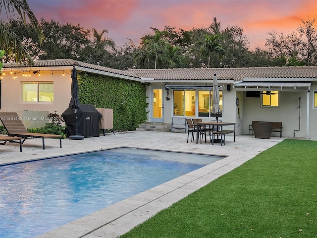 pool at dusk featuring a patio and a yard