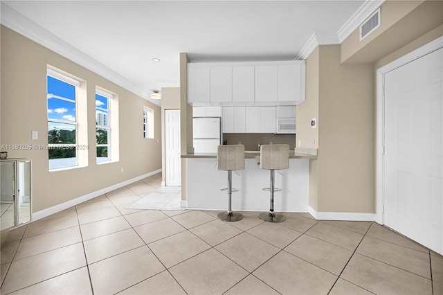 kitchen with white appliances, kitchen peninsula, a kitchen breakfast bar, white cabinets, and ornamental molding