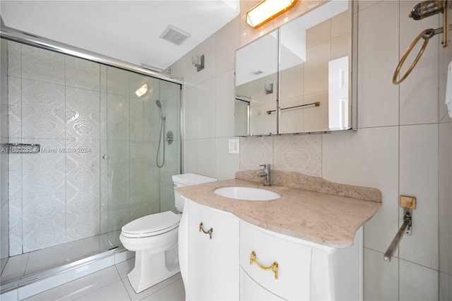 bathroom featuring toilet, tile patterned flooring, vanity, tile walls, and walk in shower