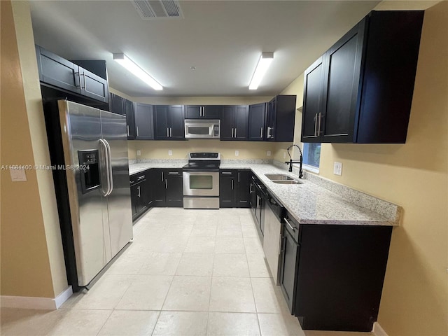 kitchen with stainless steel appliances, sink, light stone counters, and light tile patterned floors