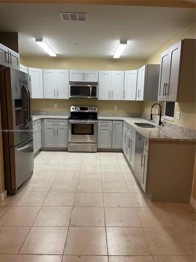 kitchen with appliances with stainless steel finishes, light stone countertops, light tile patterned flooring, gray cabinets, and sink