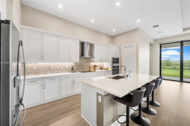 kitchen featuring white cabinetry, wall chimney range hood, appliances with stainless steel finishes, and an island with sink