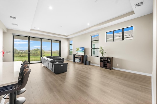 living room with light wood-type flooring and a raised ceiling