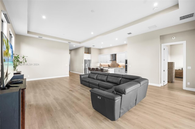 living room with light hardwood / wood-style floors and a raised ceiling