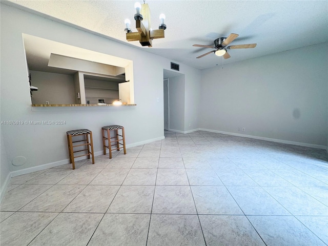 spare room featuring a textured ceiling, ceiling fan with notable chandelier, and light tile patterned floors