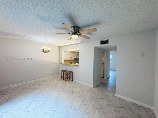 tiled spare room featuring a textured ceiling and ceiling fan with notable chandelier