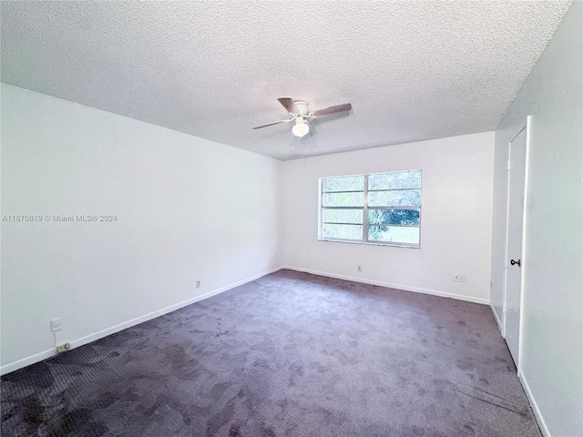 spare room with a textured ceiling, ceiling fan, and dark colored carpet