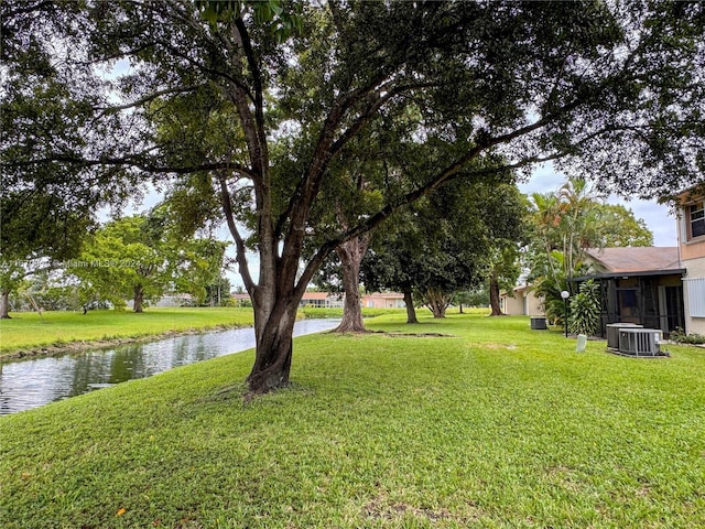 view of yard featuring central AC unit, a sunroom, and a water view