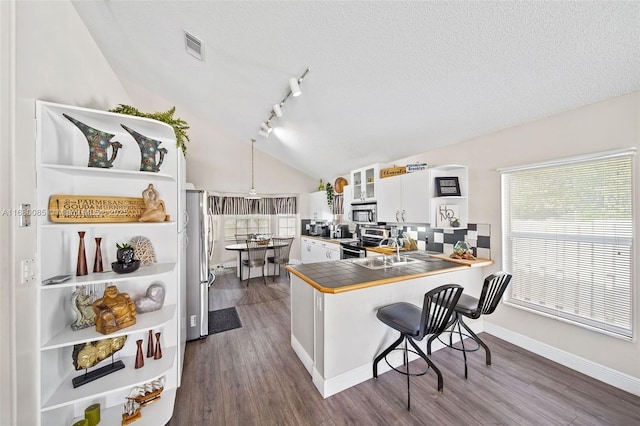 kitchen with a breakfast bar area, tile counters, stainless steel appliances, white cabinetry, and a peninsula