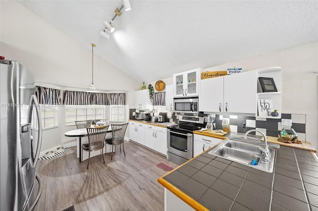 kitchen with stainless steel appliances, a sink, white cabinetry, hanging light fixtures, and glass insert cabinets