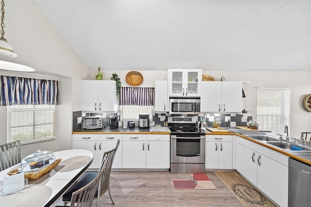 kitchen with stainless steel appliances, white cabinets, glass insert cabinets, and decorative light fixtures