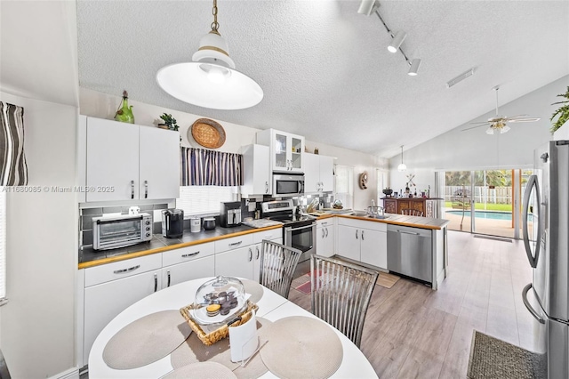 kitchen featuring white cabinetry, appliances with stainless steel finishes, light wood-type flooring, glass insert cabinets, and pendant lighting