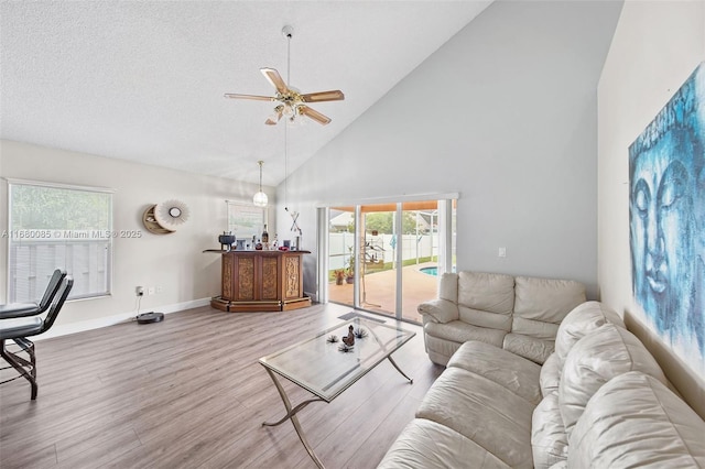 living room with ceiling fan, high vaulted ceiling, a textured ceiling, baseboards, and light wood finished floors