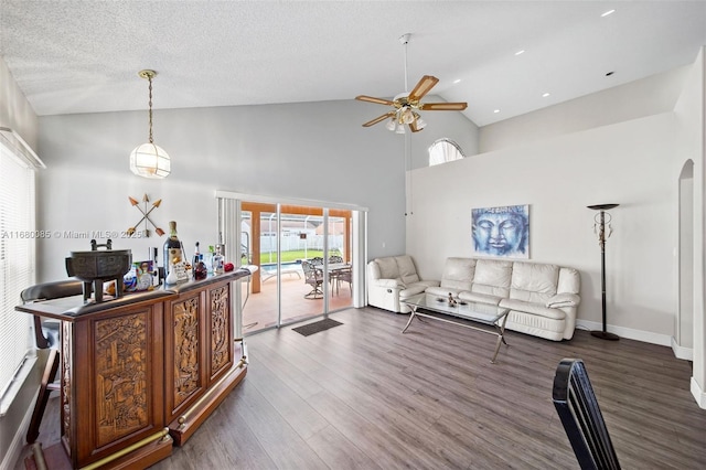 living area with arched walkways, ceiling fan, dark wood-type flooring, a textured ceiling, and high vaulted ceiling