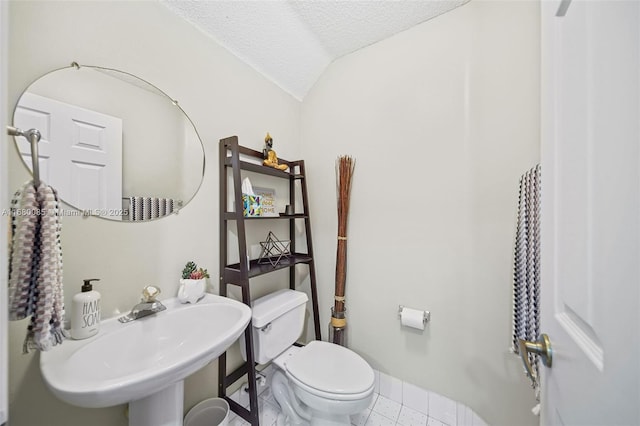 bathroom with toilet, tile patterned flooring, vaulted ceiling, a textured ceiling, and a sink