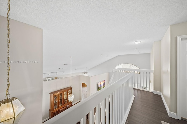 corridor with a textured ceiling, dark wood-style flooring, an upstairs landing, baseboards, and vaulted ceiling