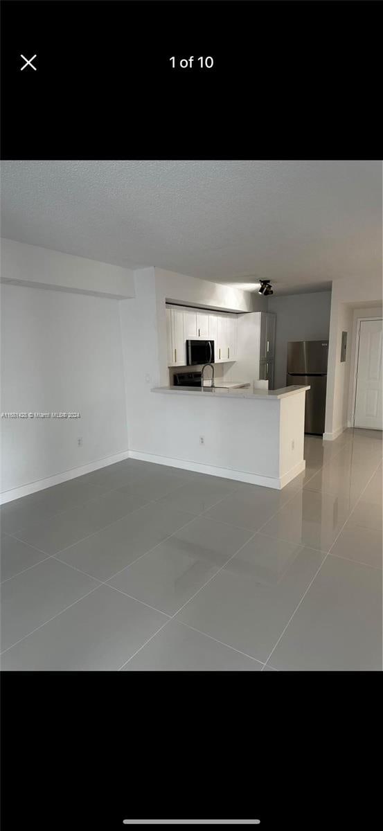 kitchen featuring tile patterned floors, kitchen peninsula, white cabinetry, a textured ceiling, and stainless steel refrigerator