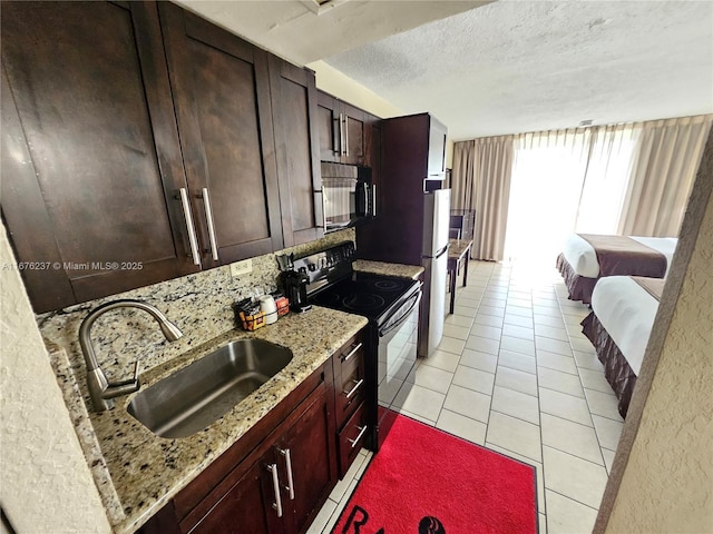 kitchen with light tile patterned floors, a textured ceiling, a sink, light stone countertops, and black appliances