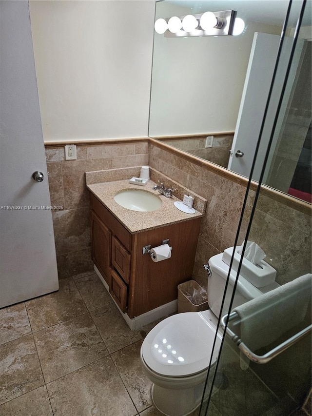 bathroom with toilet, vanity, tile walls, and wainscoting