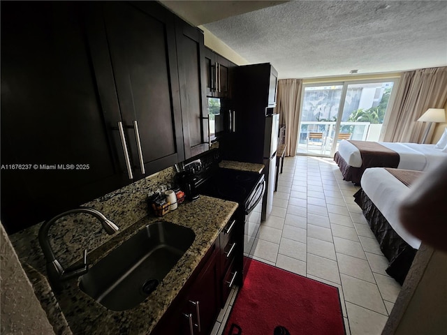 kitchen featuring black electric range, light tile patterned floors, stone countertops, a sink, and a textured ceiling