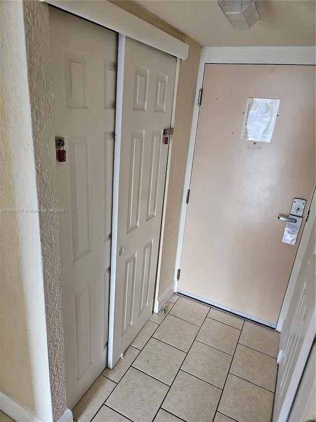 entryway featuring a textured wall, light tile patterned flooring, and baseboards