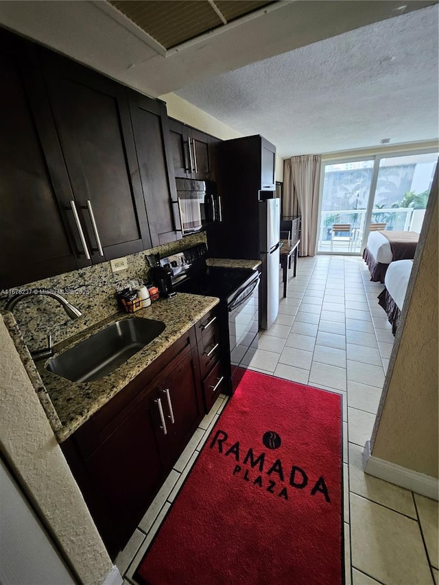 kitchen with a textured ceiling, light tile patterned flooring, a sink, light stone countertops, and black appliances