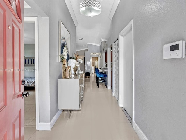 corridor featuring vaulted ceiling, ornamental molding, and light tile patterned floors