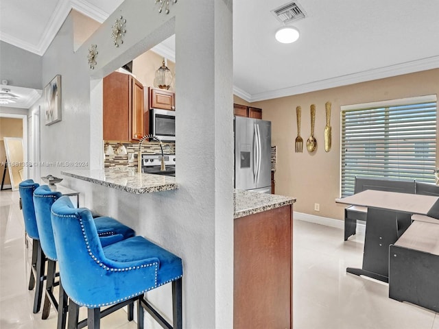 kitchen with appliances with stainless steel finishes, crown molding, backsplash, and a breakfast bar area