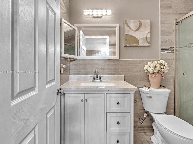 bathroom with tile walls, vanity, a shower with shower door, and toilet