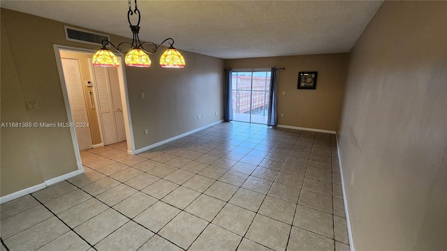 tiled empty room with a notable chandelier and a textured ceiling