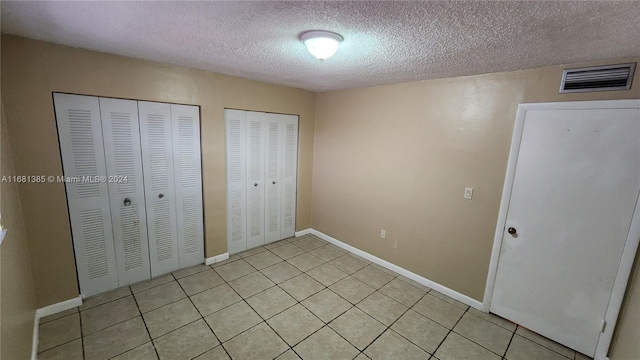 unfurnished bedroom featuring a textured ceiling, multiple closets, and light tile patterned floors