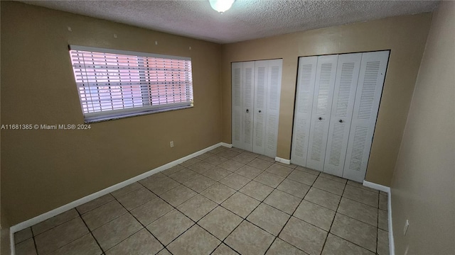 unfurnished bedroom featuring multiple closets, light tile patterned flooring, and a textured ceiling