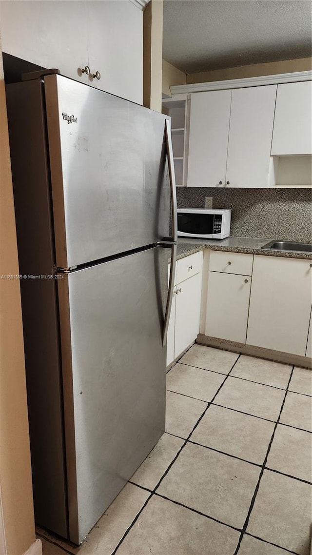 kitchen with light tile patterned flooring, sink, a textured ceiling, stainless steel fridge, and white cabinetry