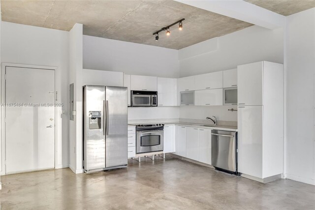 kitchen with a towering ceiling, sink, concrete flooring, stainless steel appliances, and white cabinets