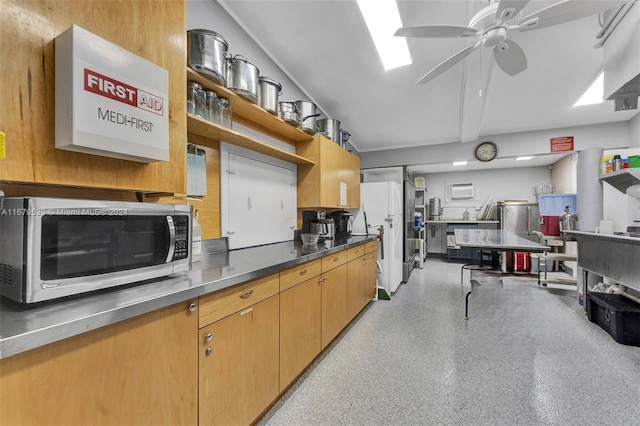 kitchen with white refrigerator, ceiling fan, and stainless steel counters