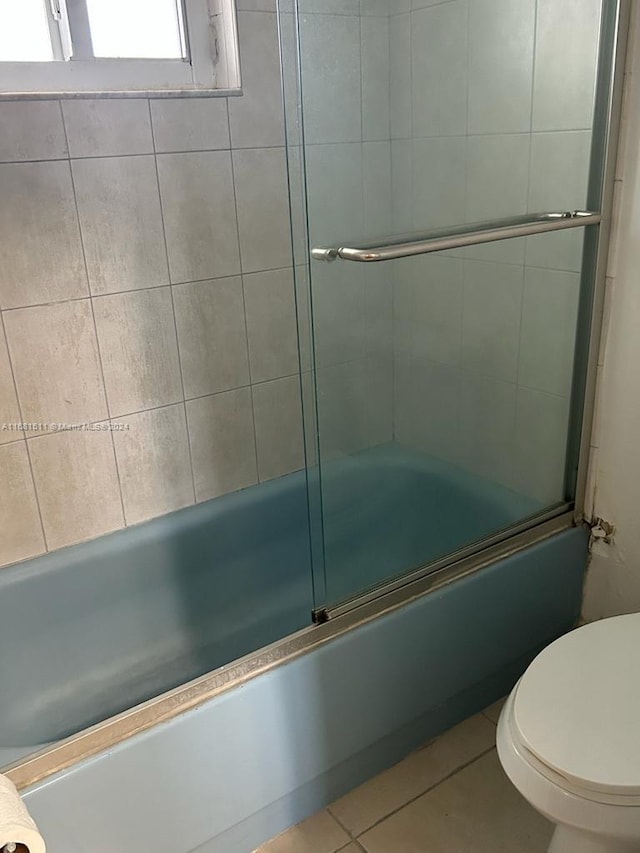 bathroom featuring toilet, combined bath / shower with glass door, and tile patterned flooring