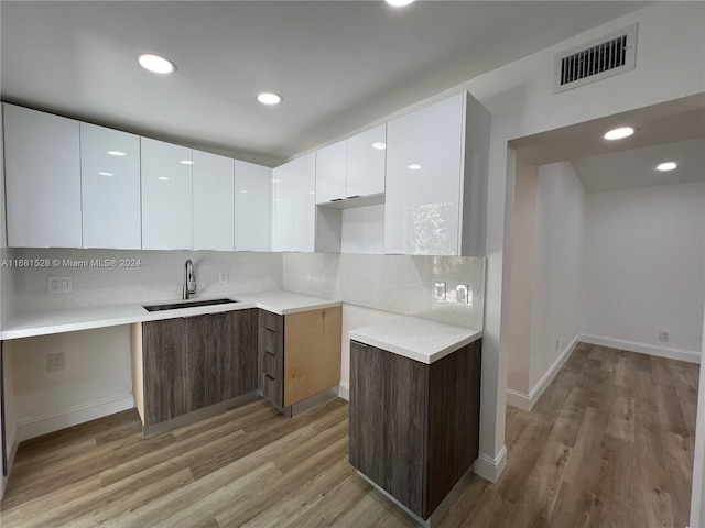 kitchen with white cabinets, dark brown cabinets, sink, and light hardwood / wood-style flooring