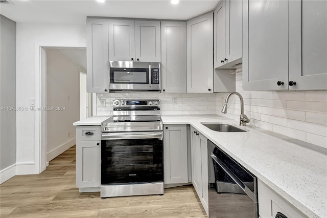 kitchen featuring light stone countertops, decorative backsplash, stainless steel appliances, sink, and light hardwood / wood-style floors