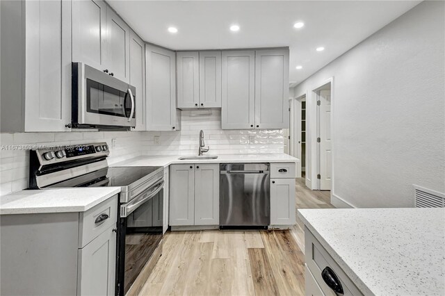 kitchen featuring backsplash, sink, light wood-type flooring, light stone counters, and stainless steel appliances