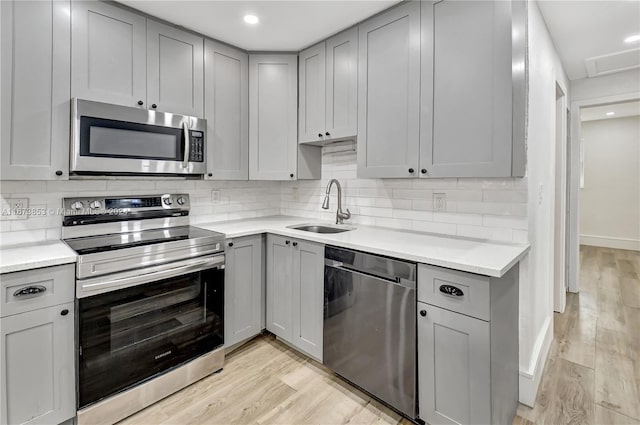 kitchen with gray cabinetry, sink, stainless steel appliances, light hardwood / wood-style flooring, and backsplash