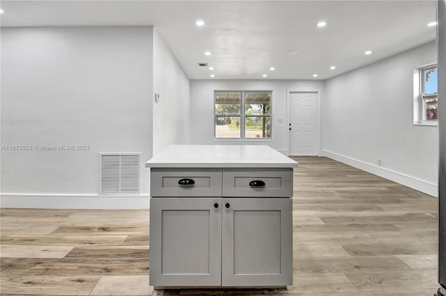 kitchen with gray cabinets, plenty of natural light, a kitchen island, and light hardwood / wood-style flooring