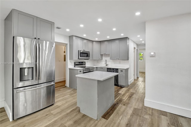 kitchen with light hardwood / wood-style flooring, backsplash, gray cabinets, a kitchen island, and appliances with stainless steel finishes