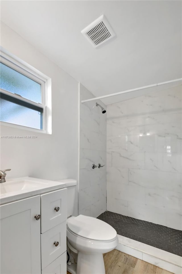 bathroom with a tile shower, vanity, wood-type flooring, and toilet