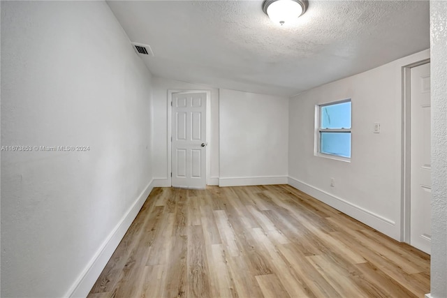 unfurnished room with light hardwood / wood-style floors, lofted ceiling, and a textured ceiling