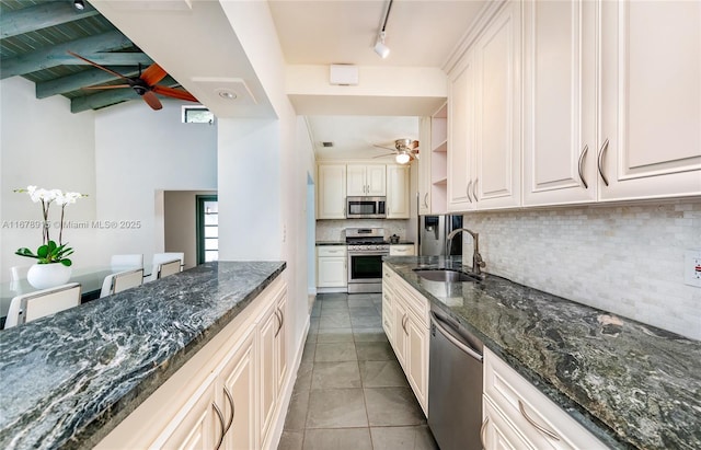 kitchen featuring decorative backsplash, dark stone counters, stainless steel appliances, sink, and beamed ceiling