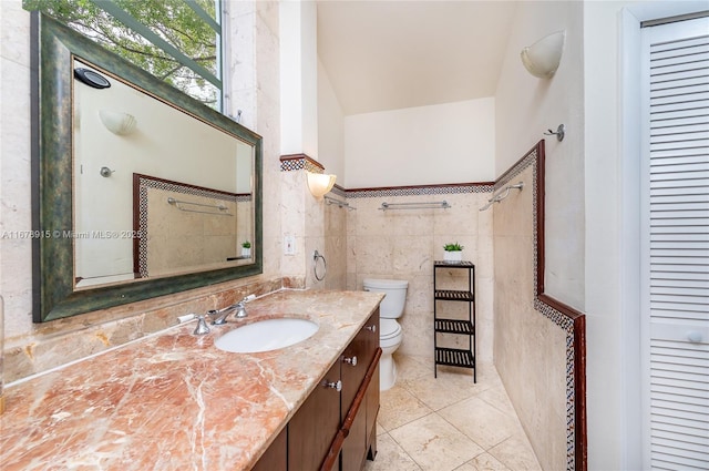 bathroom featuring tile patterned flooring, vanity, toilet, and tile walls